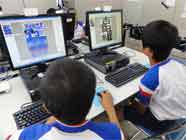 パソコンに向かって電子看板制作を体験している二人の中学生の写真